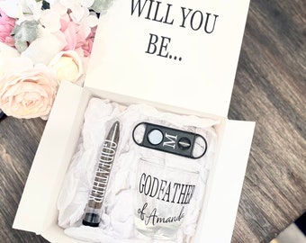 May include: A white gift box with a black lid that says "Will You Be..."  The box contains a glass with the text "Godfather of Amanda", a cigar cutter, and a cigar.