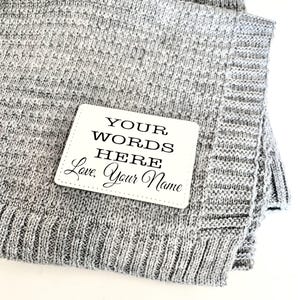 May include: A gray knitted blanket with a white tag that says "YOUR WORDS HERE Love, Your Name"
