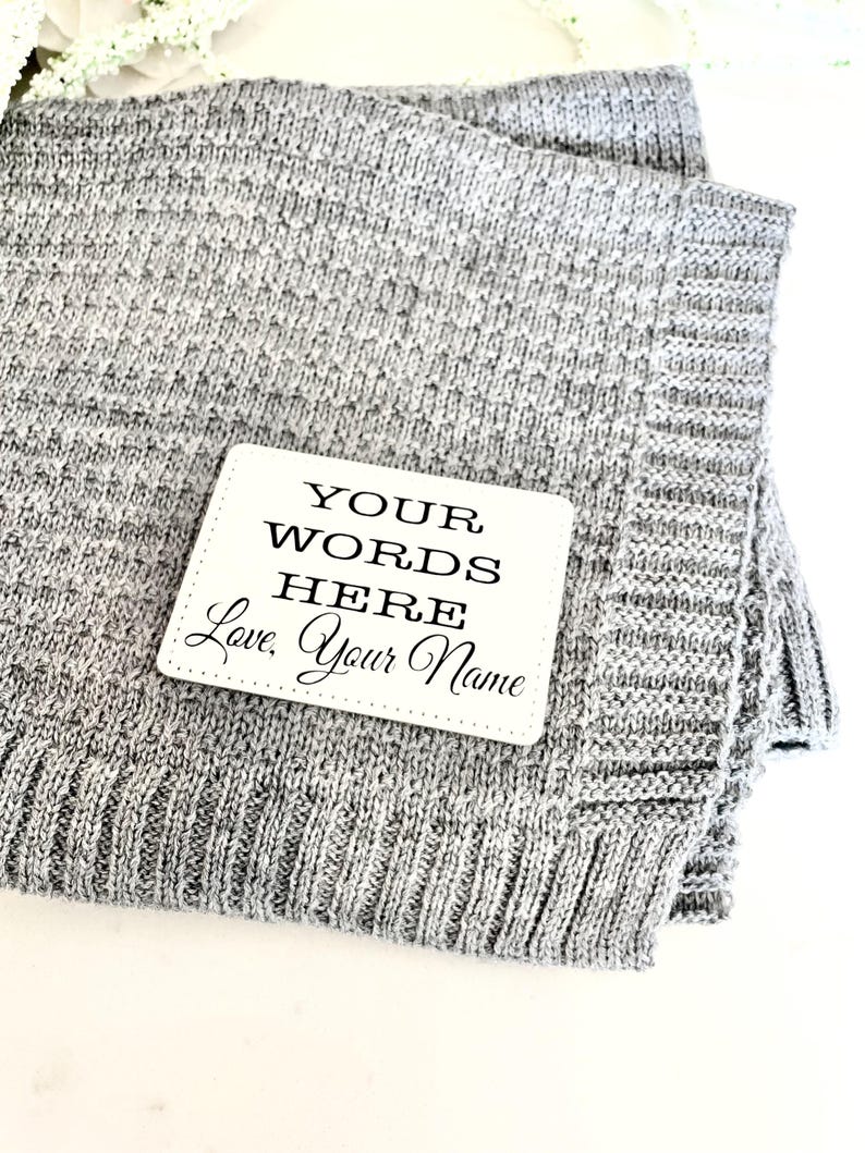 May include: A gray knitted blanket with a white tag that says "YOUR WORDS HERE Love, Your Name"