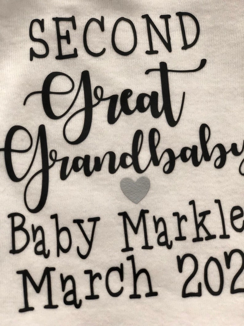 May include: White onesie with black text that reads "Second Great Grandbaby Baby Markle March 2022". A small gray heart is to the right of the text.