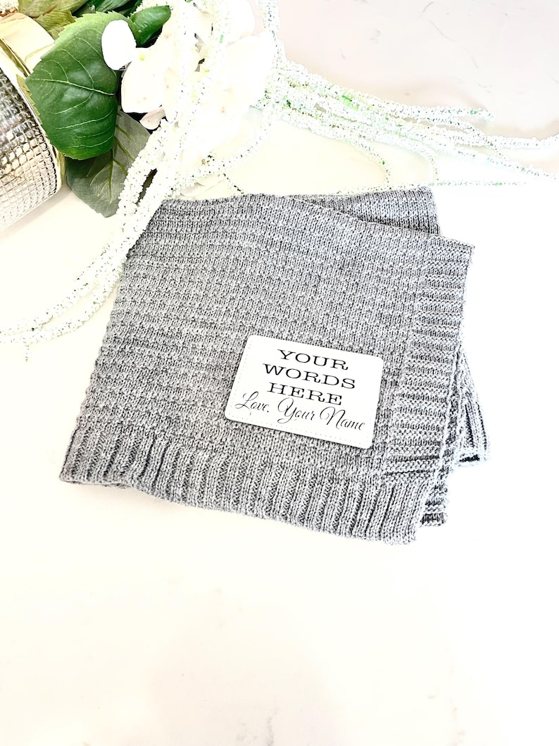 May include: A gray knitted blanket with a white square tag that says "YOUR WORDS HERE Love, Your Name".