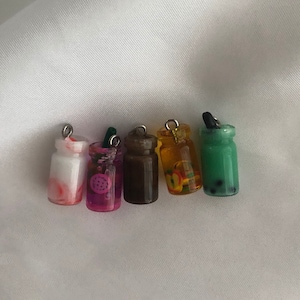 May include: Six miniature glass jars with different colored liquids and decorative elements inside. The jars are on a white background and have silver tops.