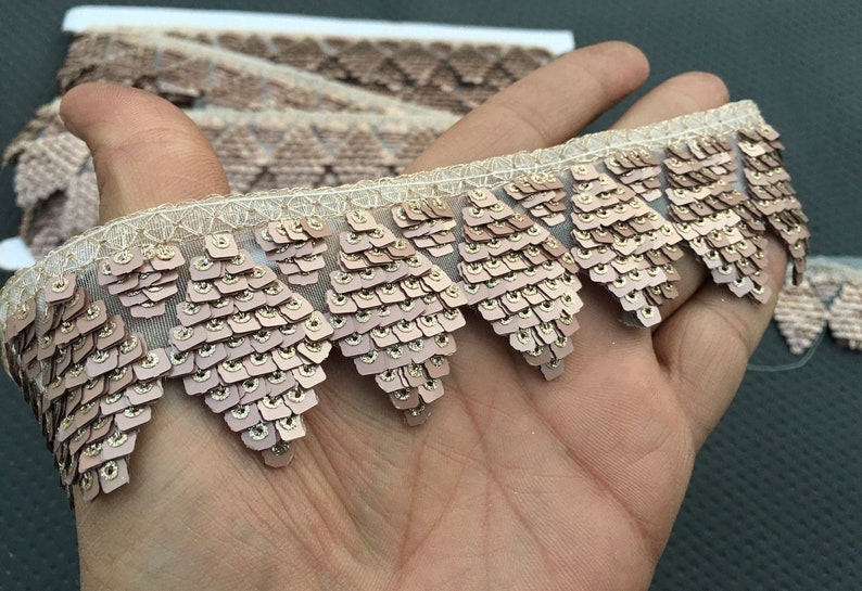 Puede incluir: Primer plano de un ribete de lentejuelas doradas y rosas con un borde festoneado. El ribete est&aacute; hecho de una tela transparente con un patr&oacute;n delicado.