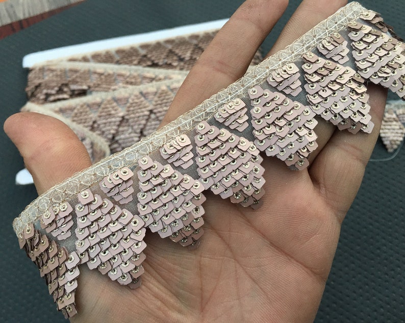 Puede incluir: Primer plano de un ribete delicado y con lentejuelas con un borde festoneado. El ribete est&aacute; hecho de una tela transparente con peque&ntilde;as lentejuelas iridiscentes de color rosa claro.