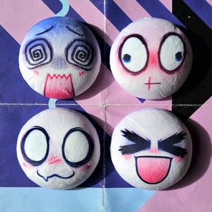May include: Four round, white plushies with expressive cartoon faces. One is blue with a distressed expression, another has wide eyes and red cheeks, a third has a surprised look, and the last has a wide grin with a pink tongue. Each has a small blue string.