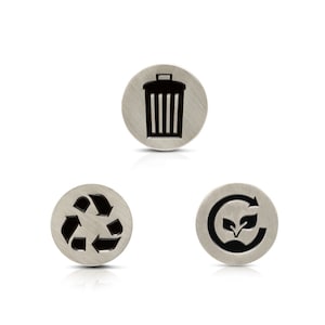 May include: Three round, brushed metal buttons with black icons. One features a trash can, another a recycling symbol, and the last a recycling arrow with leaves. The buttons are on a white background.