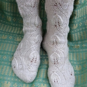 May include: A pair of white knitted socks featuring a delicate leaf pattern. The socks are crafted from fine yarn and have a soft, comfortable feel.