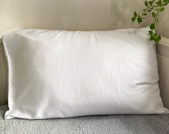 May include: A white pillow on a gray fuzzy surface. The pillow is smooth and has a slight sheen.