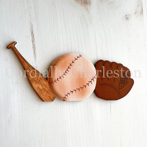May include: Wooden baseball, bat, and glove painted in brown, tan, and red. The baseball has red stitching. The glove has a white mesh insert.