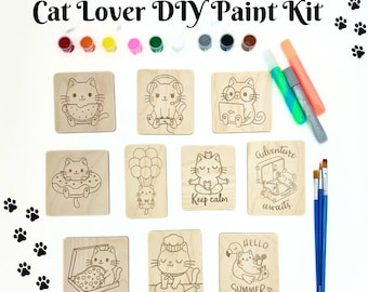 May include: A DIY paint kit featuring nine wooden squares with cute cat illustrations. The kit includes paint, paintbrushes, and markers. The illustrations include cats with donuts, cats with pizza, cats with hot air balloons, cats meditating, and cats with suitcases. The text on the squares reads "Keep calm", "Adventure awaits", and "Hello Summer".