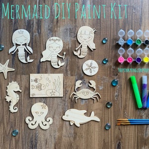 May include: A mermaid-themed DIY paint kit with wooden cutouts of a mermaid, seahorse, octopus, dolphin, crab, starfish, and a scene with fish. The kit includes paints, paintbrushes, and glitter glue.