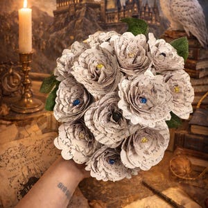 May include: A bouquet of paper flowers with text printed on the petals. The flowers have yellow and blue gem centers. The background includes a castle, an owl, books, and a candle.