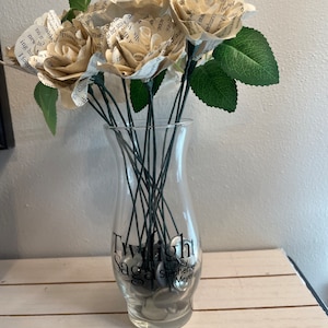 May include: A bouquet of paper roses made from book pages in a clear glass vase with the words "Twilight Saga by Stephenie Meyer" printed on the vase.
