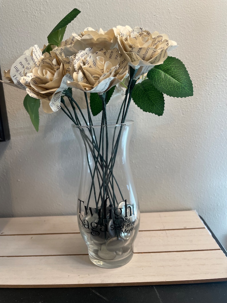 May include: A bouquet of paper roses made from book pages in a clear glass vase with the words "Twilight Saga by Stephenie Meyer" printed on the vase.