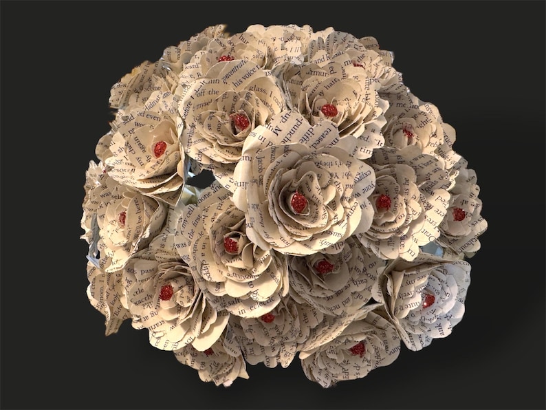 May include: A bouquet of paper flowers made from book pages. The flowers are white with red centers. The bouquet is arranged in a circular shape.