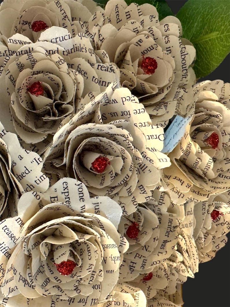 May include: A bouquet of paper roses made from old book pages. The roses are cream colored and have red glitter accents.