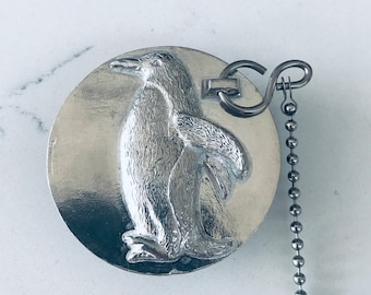 Peut inclure: Bouchon de bouteille en argent en forme de pingouin avec une chaîne. Le pingouin est détaillé et a une surface texturée.