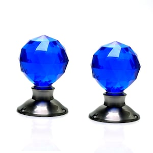 Puede incluir: Dos pomos de puerta de cristal azul con bases plateadas. Los pomos son facetados y tienen un acabado brillante.