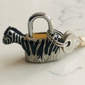 Puede incluir: Un candado de plata con forma de cebra con un patrón de cebra blanco y negro y una llave de plata adjunta.