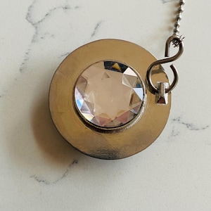 May include: A decorative ceiling fan pull chain with a large, faceted, clear crystal gem set in a round, brushed silver-tone metal bezel. A silver-tone chain and connector complete the design. The pull chain is designed to add a touch of elegance.