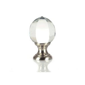May include: A clear crystal finial with a faceted design, mounted on a silver base. The finial is a decorative element for curtains or drapery.
