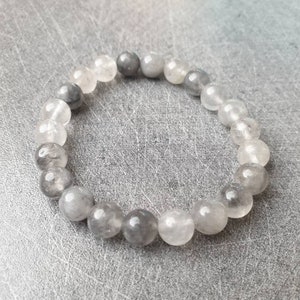 Könnte beinhalten: Ein graues und klares Kristall-Armband. Das Armband besteht aus runden Perlen mit einer glatten, polierten Oberfläche.