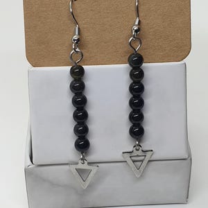 May include: A pair of dangle earrings featuring black beads and silver-colored triangle charms. The earrings have a simple design with a hook closure. The beads are strung together, and the triangle charm hangs at the bottom.