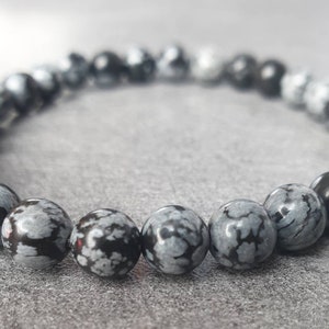 Könnte beinhalten: Ein Armband aus schwarzen und weißen, gefleckten Steinperlen. Die Perlen sind rund und haben eine glatte, polierte Oberfläche.