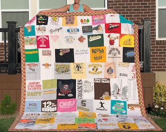 May include: A handmade quilt composed of various t-shirts, featuring a patchwork design. The quilt showcases a variety of colors and graphics from different events and organizations. The border is a patterned fabric with a red and pink trim. The quilt is approximately 70 inches wide and 80 inches long.