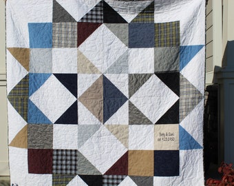 May include: A white quilt with a patchwork design featuring various shades of blue, gray, brown, and red fabrics. The quilt is made up of triangles and squares, and the center features a large white square with the text "Sissy & Earl est. 12.31.1950".