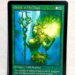 May include: A Magic: The Gathering card featuring the "Oracle of Mul Daya." The card has a green background with an illustration of a female elf shaman holding a staff. Text includes the card's name, mana cost, creature type, and abilities.