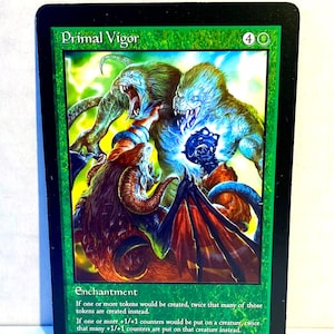 May include: A green Primal Vigor card with a fantasy illustration of monstrous creatures. The card features the text "Primal Vigor" at the top and "Enchantment" at the bottom, along with game rules. The artwork depicts a chaotic scene with vibrant colors.