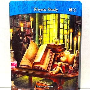 May include: A trading card titled "Rhystic Study" features a detailed illustration of a study with a black cat, open books, candles, and a small doll. The card has a blue border and text that reads "Enchantment".