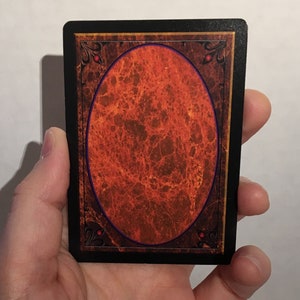 May include: A black card with a gold border and a red and orange oval in the center. The oval has a blue border and a marbled texture.