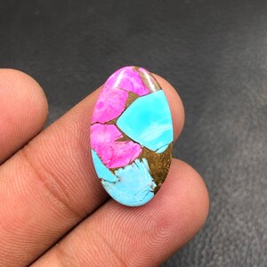 Può includere: Una gemma ovale con un motivo a mosaico. La pietra presenta colori vivaci, tra cui rosa, turchese e oro. Le sezioni rosa e turchese sono intervallate da venature color oro, creando un design unico e accattivante.