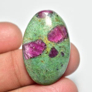 Peut inclure: Pierre précieuse ovale avec une matrice verte et d'étonnantes inclusions de rubis magenta. La pierre polie présente un mélange de couleurs et de textures, idéale pour la joaillerie ou la collection. Mesure environ 3 cm.