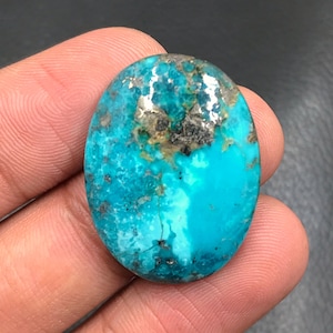 Può includere: Un cabochon ovale in turchese blu brillante con una matrice di pirite nera e argentata. La pietra ha una superficie liscia e lucida.