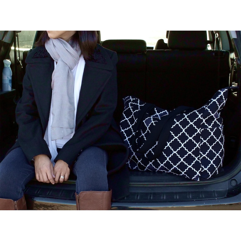 May include: A black and white patterned tote bag with a geometric design sits in the back of a car. The bag is large enough to hold many items.