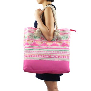May include: A large pink tote bag with a white rope handle and a colourful geometric pattern. The bag has a pink lining and a zipper closure.