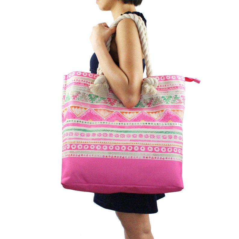 May include: A large pink tote bag with a white rope handle and a colourful geometric pattern. The bag has a pink lining and a zipper closure.