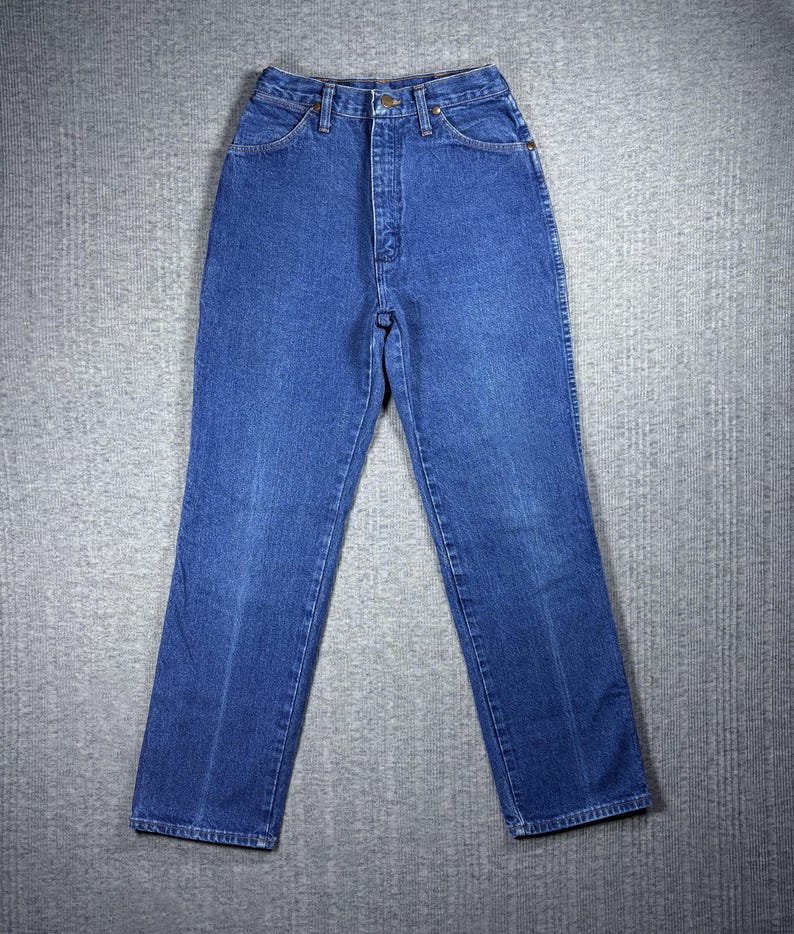 K&ouml;nnte beinhalten: Blaue Jeans aus Denim mit hohem Bund und geradem Bein. Die Jeans haben ein klassisches F&uuml;nf-Taschen-Design, einen Knopf- und Rei&szlig;verschluss sowie G&uuml;rtelschlaufen. Der Denim hat eine mittelblaue Waschung mit dezenten Ausbleichungen und Abnutzungen.