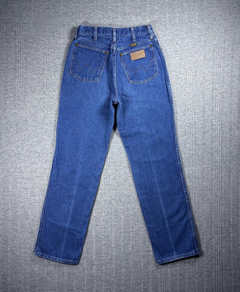 K&ouml;nnte beinhalten: Blaue Jeans aus Denim mit klassischem F&uuml;nf-Taschen-Design. Die Jeans haben einen geraden Beinverlauf und einen braunen Lederaufn&auml;her auf der Ges&auml;&szlig;tasche. Das Wrangler-Logo ist auf dem Aufn&auml;her sichtbar. Die Jeans bestehen aus strapazierf&auml;higem Denim-Stoff.