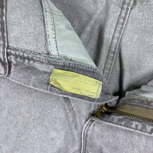 Peut inclure: Gros plan sur un jean en denim gris clair. Le jean a une fermeture &eacute;clair et une &eacute;tiquette jaune avec du texte. Le tissu semble us&eacute;, avec des coutures et des coutures visibles. Le style g&eacute;n&eacute;ral est d&eacute;contract&eacute;.