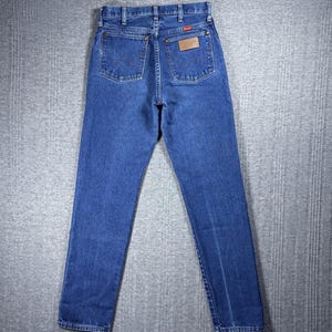 May include: Blue denim jeans with a classic five-pocket design. The jeans feature a straight leg cut and a brown leather patch on the back pocket. The jeans are made of a durable denim fabric.