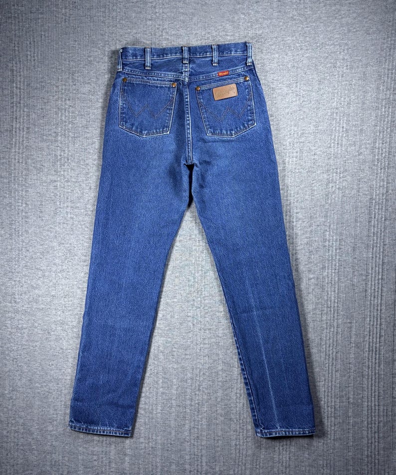 May include: Blue denim jeans with a classic five-pocket design. The jeans feature a straight leg cut and a brown leather patch on the back pocket. The jeans are made of a durable denim fabric.