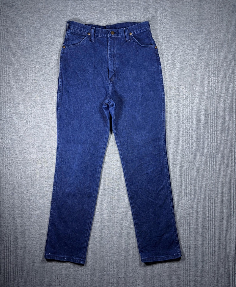 May include: Dark blue denim jeans with a classic five-pocket design. The jeans have a high waist and a straight leg cut. The denim is a solid, medium-weight fabric. The jeans are button and zipper closure.