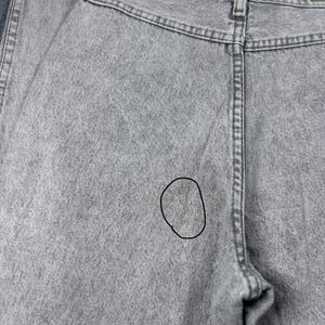Peut inclure: Gros plan du dos d'un jean en denim gris clair. Le jean a une conception classique &agrave; cinq poches avec une fermeture &agrave; bouton et &agrave; glissi&egrave;re. Le tissu a un aspect textur&eacute; et il y a une petite tache au dos.