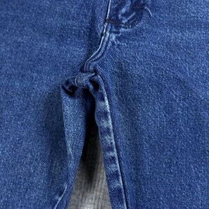 May include: Close-up of blue denim jeans, showcasing the texture and stitching details. The image highlights the fabric's weave and the construction of the garment, focusing on the seam and the area around the zipper.