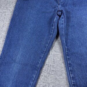K&ouml;nnte beinhalten: Nahaufnahme einer blauen Jeans. Die Jeans hat ein klassisches F&uuml;nf-Taschen-Design, einen Knopf- und Rei&szlig;verschluss und der Markenname "Wrangler" ist auf dem Bund sichtbar. Der Denim hat ein leicht verwaschenes Aussehen.
