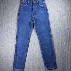 May include: Classic blue denim jeans with a straight leg cut. The jeans feature a button and zipper closure, front and back pockets, and belt loops. The denim is a medium wash, and the jeans are laid flat on a gray surface.